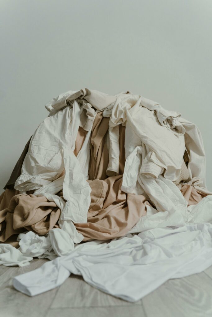 pexels photo 8453415 8453415 A heap of beige and white clothes casually piled on a wooden floor.
